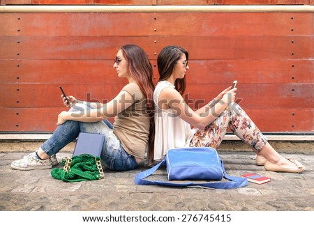 Hipster couple of girlfriends in disinterest moment with mobile smart phones - Concept of relationship apathy sadness and isolation using new technologies - Female friends with smartphones addiction
