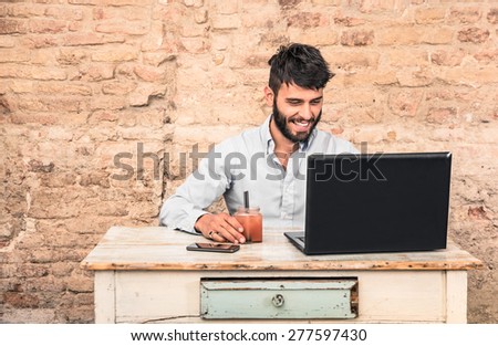 Young hipster guy with mustache sitting at vintage desk with laptop computer in grunge alternative office - Concept of start up business enjoying working hours - Soft retro desaturated filtered look