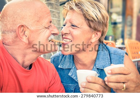 Happy playful senior couple in love tenderly enjoying a cup of coffee - Joyful elderly active lifestyle - Man having fun and smiling with her wife in bar cafe restaurant during evergreen vacation