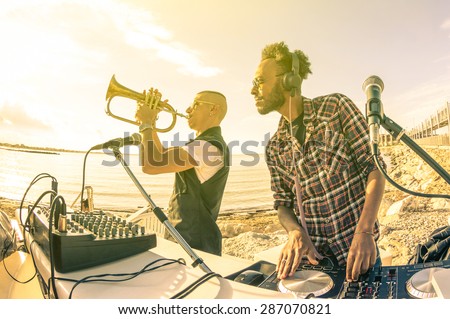 Dj playing summer hits at sunset beach party with trumpet jazz performer - Vacation concept at open air club with house music groove location - Warm vintage sunshine filter with backlight soft focus