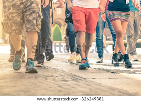 Crowd of people walking on the street - Detail of legs and shoes moving on sidewalk in city center - Travelers with multicolor clothes on vintage filter - Shallow depth of field with sunflare halo