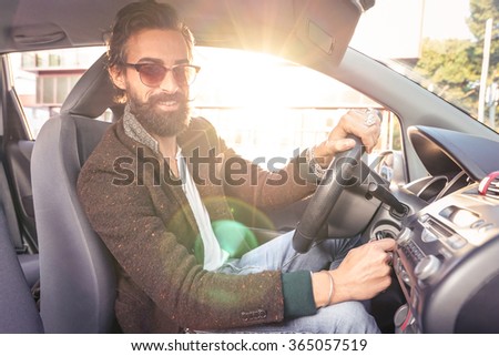 Young hipster fashion model driving car - Young confident man with beard and alternative mustache smiling looking at camera - Lens flare halo is part of composition - Soft vintage marsala filter