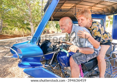 Happy senior couple having fun with tricycle in Philippines travel - Concept of active playful elderly during retirement - Everyday joy lifestyle without age limitation - Warm afternoon color tones