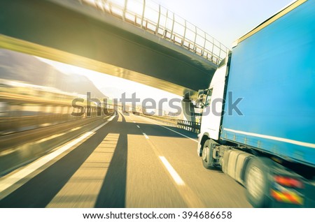 Blurred motion of semi truck speeding on highway under overpass - Transport logistic with semitruck container driving on speedway - Soft vintage filter with sunshine halo - Focus on further street end