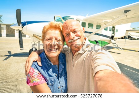 Happy senior couple taking selfie with private ultralight plane at tour around world - Elderly concept with active retired people enjoying pension moments - Warm bright sunny afternoon color tones