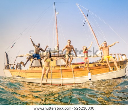Frontal view of young multiracial friends jumping from wooden sailing boat on sea trip - Rich happy guys and girls having fun in summer party day - Exclusive vacation concept - Warm vintage filter