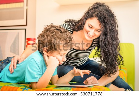 Young mother having fun with son using tablet on bed - Learning computer tech with sister in children room - Teacher showing boy how to interact on modern device - Vivid filter with focus on kid face