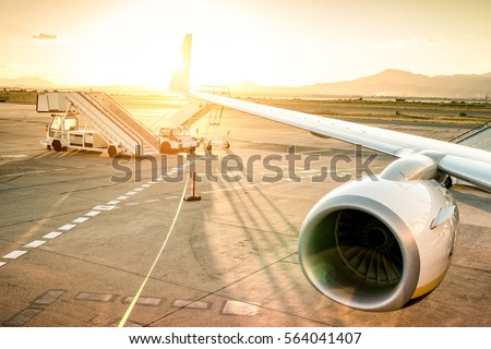 Airplane at international airport ready for takeoff - Modern terminal gate at sunset - Travel trip concept around the world - Wide angle with warm vignetting filter and enhanced sunshine lens flare