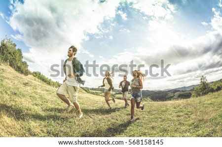 Group of friends running free on grass meadow - Friendship and freedom concept with young happy people moving free at camping experience - Vintage desaturated filter with backlight contrast sunshine