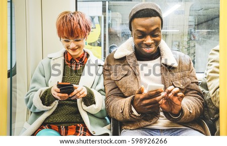 Multiracial hipster friends couple having fun with smartphone in subway train - Urban relationship concept with young people watching mobile phone in city underground area - Bright desaturated filter