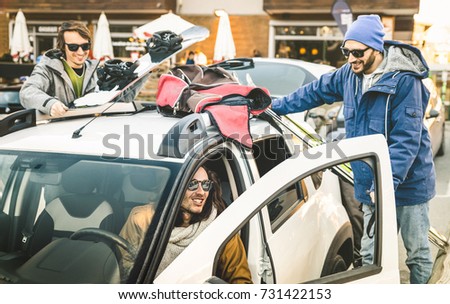 Best friends having fun together preparing car for ski and snowboard at mountain trip - Friendship hangout concept with young people loving winter sports travel - Vintage desaturated contrast filter