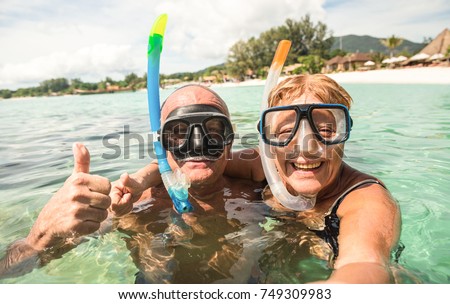 Senior happy couple taking selfie in tropical sea excursion with water camera - Boat trip snorkeling in exotic scenarios - Active retired elderly and fun concept around the world - Warm bright filter
