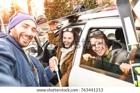 Best friends having fun taking selfie at car with ski and snowboard on mountain trip - Friendship hangout concept with young people loving winter sports travel - Vintage desaturated contrast filter