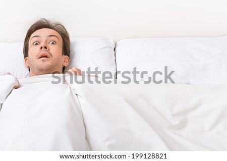 Young man lies in the bad and looks at camera with scared view