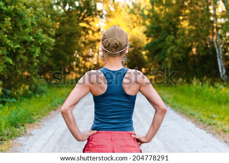 Young sport woman with muscular back stays on the road in the forest