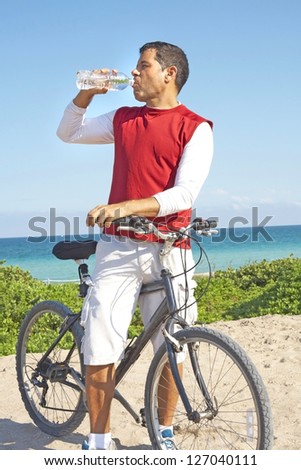 Mid adult man in casual t-shirt on bicycle drinking water from bottle. Vertical shot.