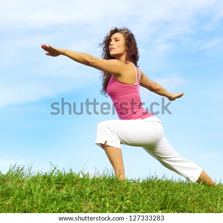 young beautiful girl doing yoga in warrior pose on a beautiful day with clear blue sky.
