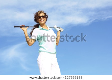 pretty female golfer relaxing holding golf club against clear blue sky. Female golfer wearing sunglasses.