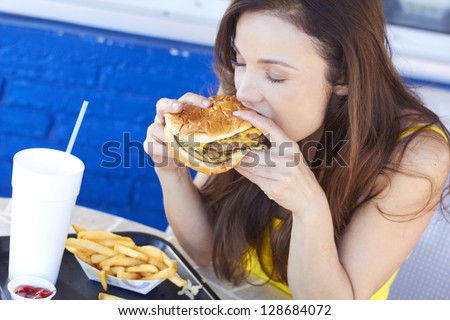 Beautiful young lady eating a tasty burger at an outdoor cafe. Horizontal Shot.