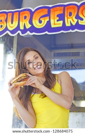 Portrait of a happy young woman posing with a hamburger. Vertical Shot.