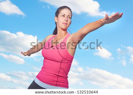 Healthy young woman doing yoga warrior pose against cloudy sky. Horizontal Shot.