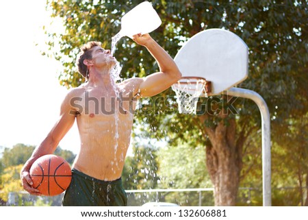 Young man on basketball court hydrating himself with a gallon of water.
