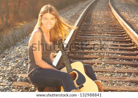Happy Beautiful Young Woman With Guitar On Railroad Tracks. Copy Space. Pretty smiling young lady holding guitar on railway.
