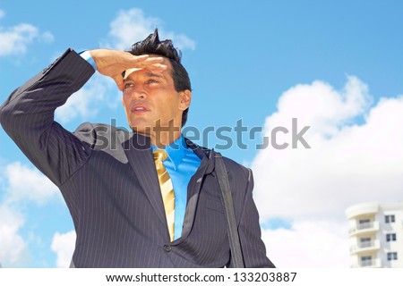 Confident young businessman shielding eyes for better vision against cloudy sky. Horizontal shot.