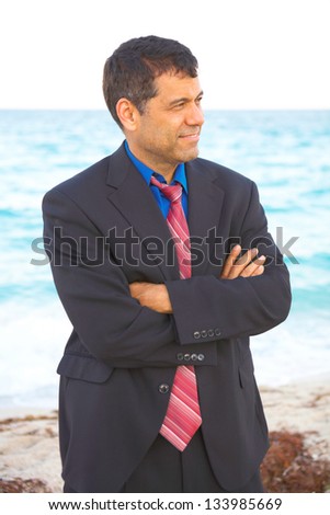 Mid adult mixed race businessman looking away while standing arms crossed with sea in background. Vertical shot.