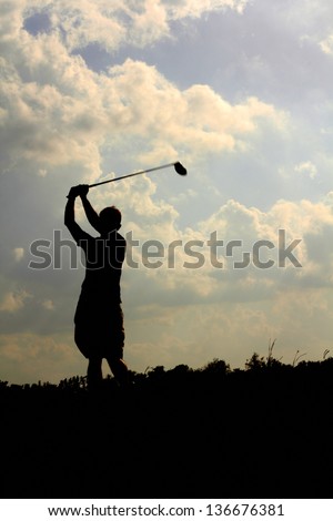 Silhouette of male golfer swings to a hit golf ball. Vertical shot.