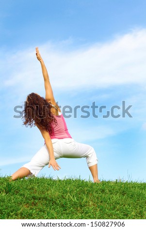 young beautiful girl doing yoga in warrior pose on a beautiful day with clear blue sky.