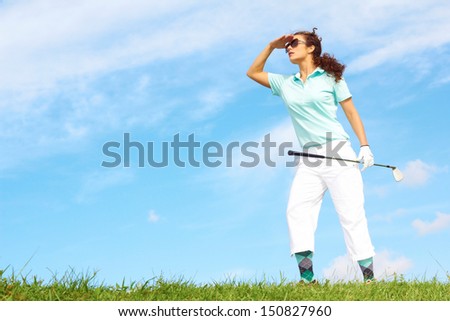 Lost female golfer holding golf club looking for golf ball against clear blue sky. Wearing Sunglasses.
