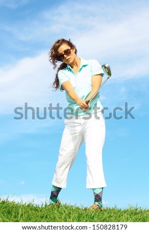 Pretty female golfer taking a golf swing in the rough.