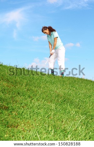 Pretty female golfer taking a golf swing in the rough.