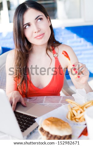 beautiful latin girl thinking about eating fast food while working on laptop