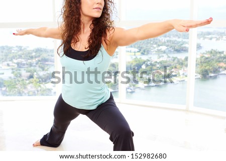 Young beautiful female doing yoga warrior pose in sky rise gym with copy space.