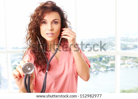 Close-up of a happy friendly beautiful nurse holding stethoscope about to check a heartbeat