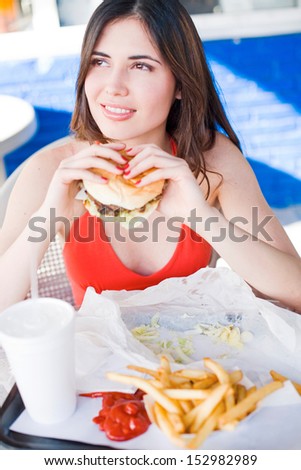 Beautiful happy young latin girl eating hamburger at fast food restaurant