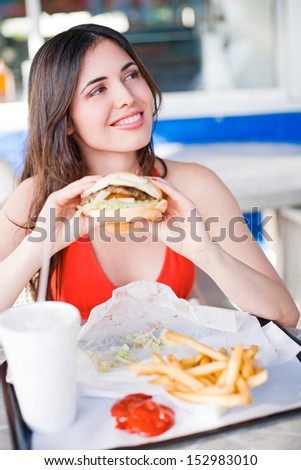 Beautiful happy young latin girl eating hamburger at fast food restaurant