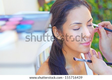 Makeup artist using a brush to apply makeup to an attractive young woman\'s eyelids. Horizontal shot.