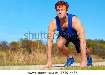 Handsome runner man at the start in stance. Copy space, color image, young man in sports wear about to run on a beautiful day in nature. Horizontal