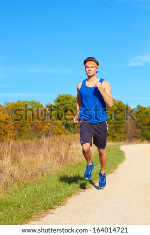 Handsome man jogging on nature trail near forest preserve. Color image, copy space, male jogger running outside on a beautiful day in nature.