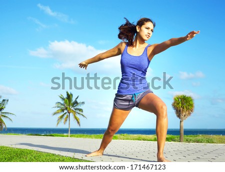 young beautiful mixed race girl doing yoga warrior pose on a beautiful day with clear blue sky. Pretty hispanic female performing relaxation exercise on a nice spring day. Color image, copy space.