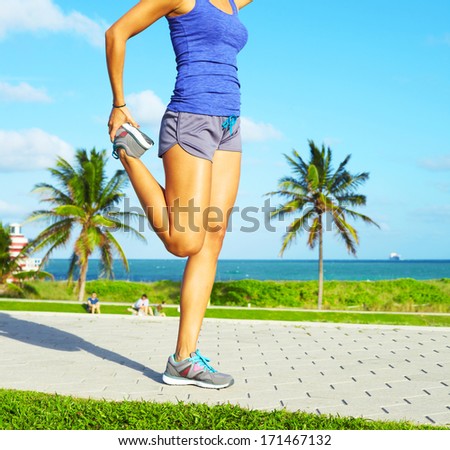 healthy young pretty mixed race woman stretching her leg during exercise on running trail near ocean right before a work out.
