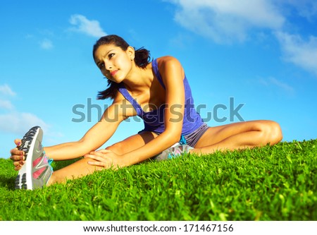 healthy young pretty mixed race woman stretching her leg during exercise in grass right before a work out Horizontal shot healthy young pretty mixed race woman stretching her leg during exercise in grass right before a work out Horizontal shot