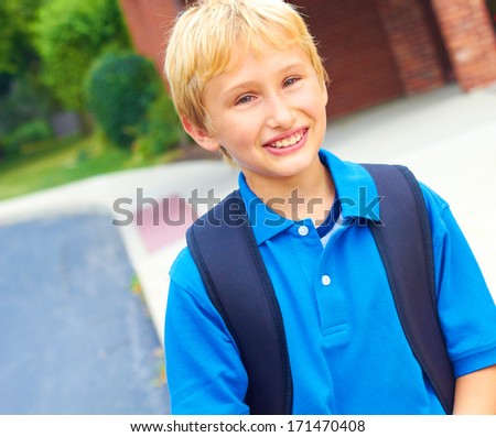 Happy young student going back to school carrying backpack. Cheerful school boy standing  in front of school building smiling and confident. Color Image, copy space.