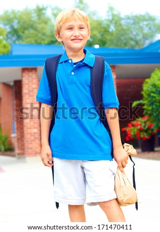 Happy young student going back to school carrying backpack. Cheerful school boy standing  in front of school building smiling and confident. Color Image, copy space.
