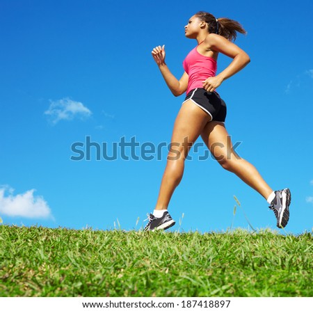 Sporty mixed race woman jogging. Color image, copy space, african american ethnicity female running with green grass and blue sky.