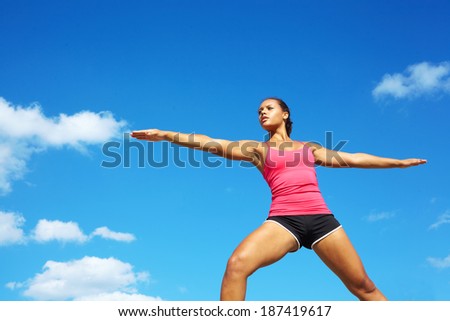young beautiful mixed race girl doing yoga warrior pose on a beautiful day with clear blue sky. Pretty african american female performing relaxation exercise on a nice spring day. copy space.