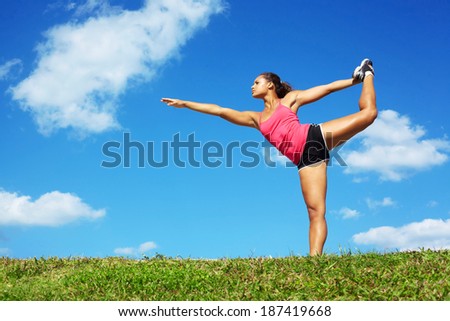 young beautiful mixed race girl doing yoga warrior pose on a beautiful day with clear blue sky. Pretty african american female performing relaxation exercise on a nice spring day. copy space.